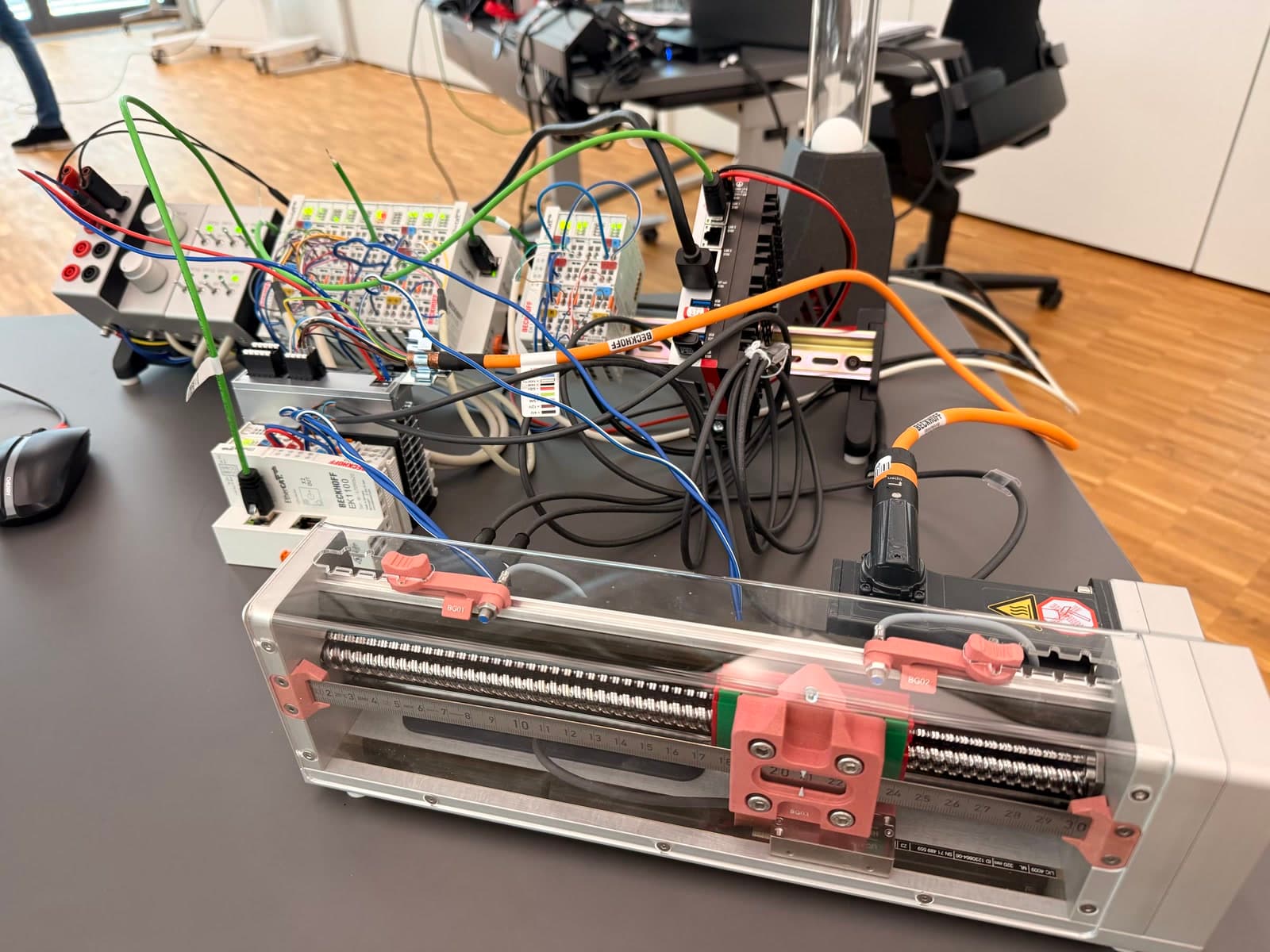 Physical Beckhoff linear-axis test setup with EtherCAT control hardware and end-position sensors.